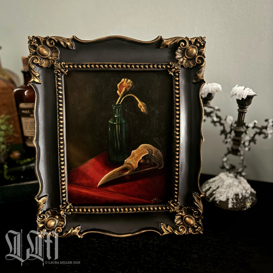 Decorative still life painting in a baroque style, with a crow skull and dried yellow flowers in vintage green bottle. Framed in ornate black and gold antique style picture frame.