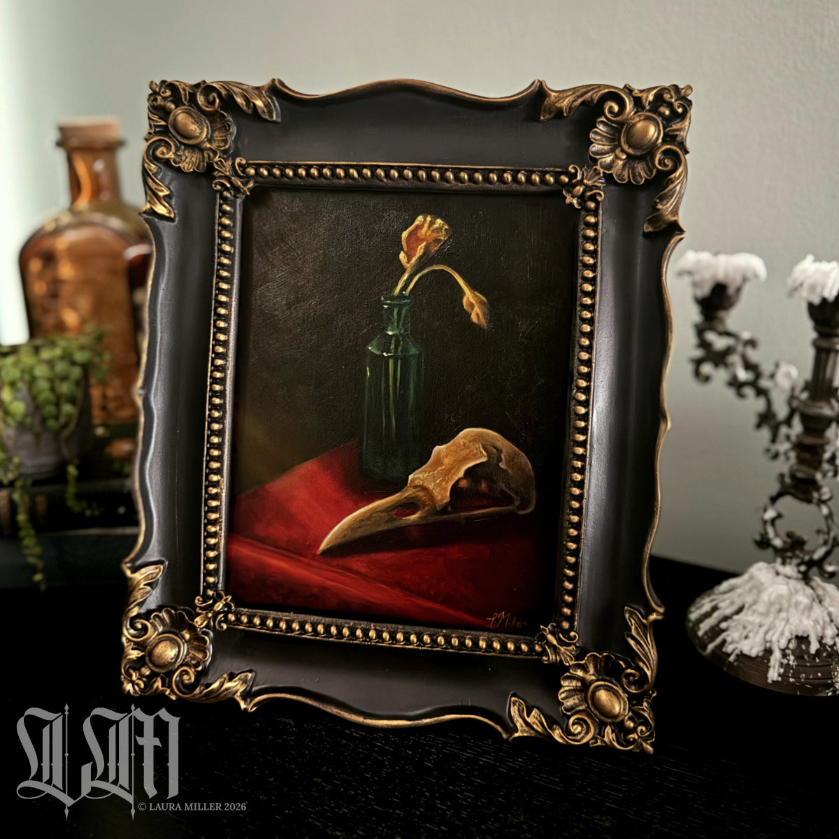 Decorative still life painting in a baroque style, with a crow skull and dried yellow flowers in vintage green bottle. Framed in ornate black and gold antique style picture frame.